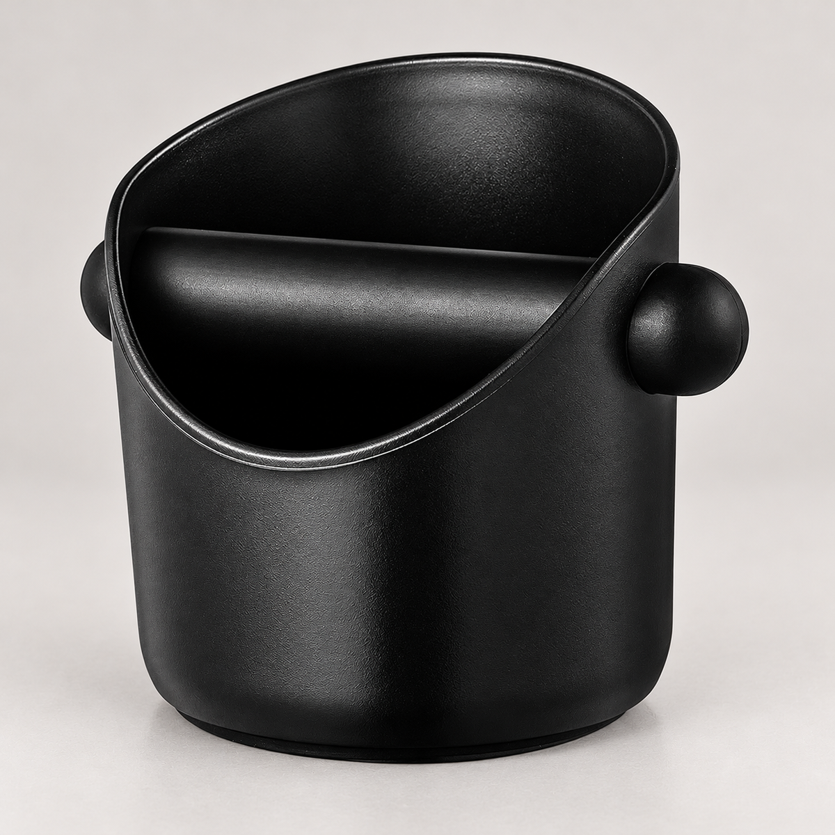 Compact black espresso knock box with rubber knock bar — warm grey background