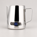 Stainless steel milk jug with temperature indicator — warm grey background
